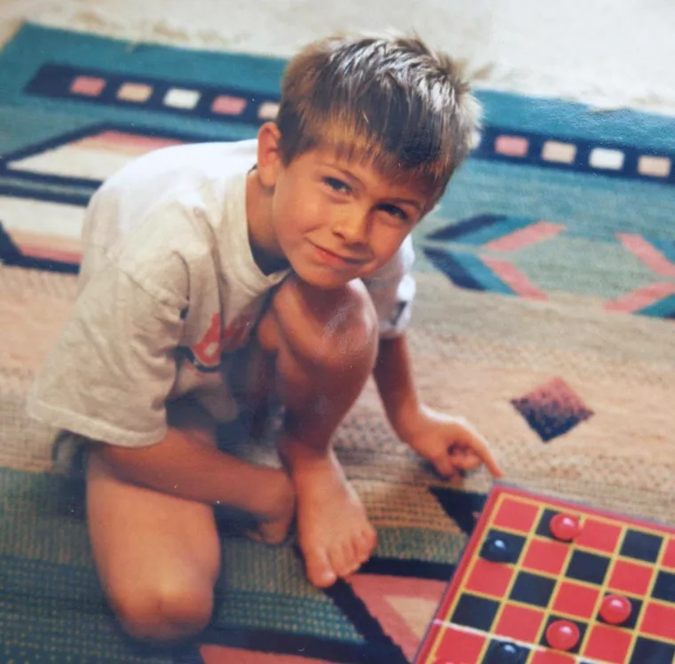 David at nine years old, kneeling on a patterned rug over a checkers board.