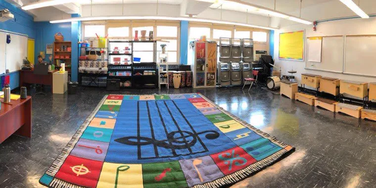 An empty elementary music room, with a large treble-clef rug in the middle of the floor.